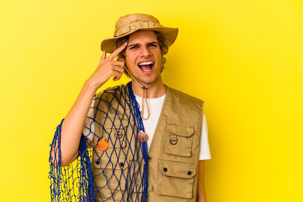 Young fisherman with makeup holding a net isolated on yellow background  showing a disappointment gesture with forefinger.