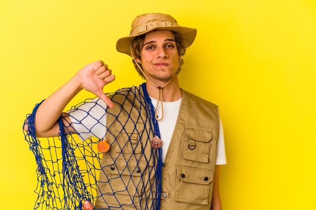 Young fisherman with makeup holding a net isolated on yellow background  showing a dislike gesture, thumbs down. Disagreement concept.