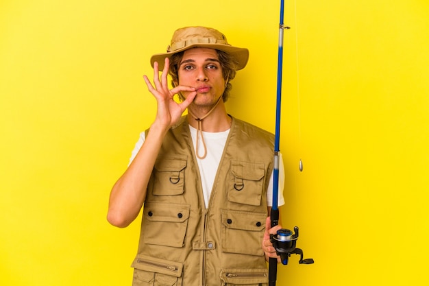 Young fisherman with makeup holding rod isolated on yellow background  with fingers on lips keeping a secret.
