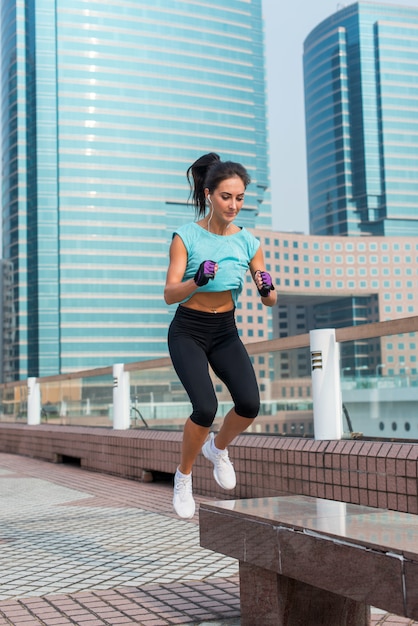 Young fit active woman bench jump squat jumping on city street. Fitness girl doing exercises outdoors.