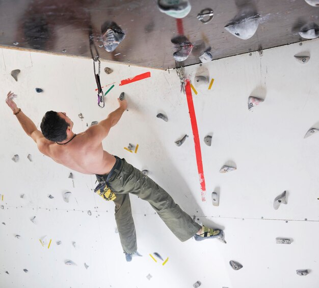 L'uomo giovane e in forma esercita l'arrampicata libera in montagna sulla parete pratica indoor