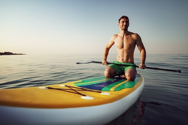 Young fit man on paddle board floating on lake