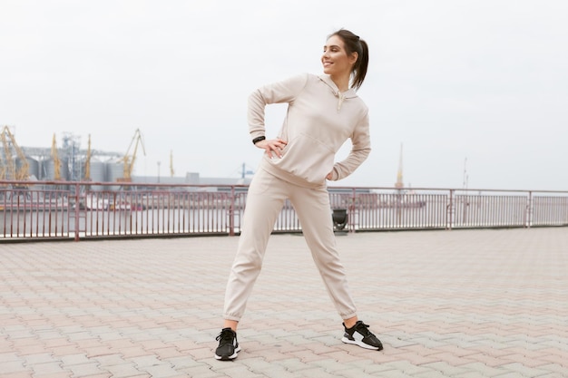 Young fit slim woman doing warmup exercise before training outdoors