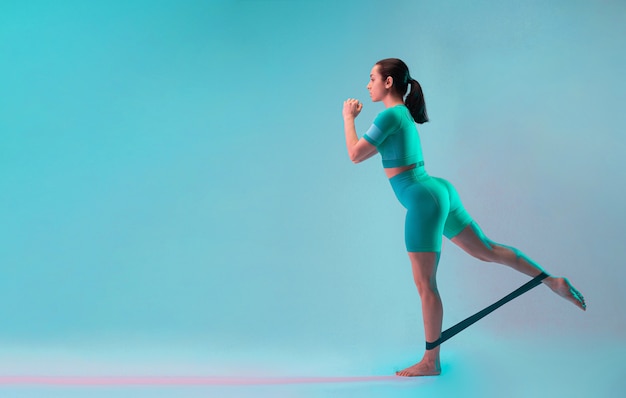 Young fit and sportive woman with resistance band for legs on gradient background. Fit sportswoman posing. Perfect body ready for summertime. Beauty, resort, sport concept.