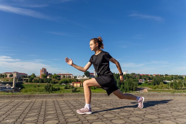 都会の公園でトレーニング後にストレッチする黒い服を着た若いフィット感とスポーティな女の子フィットネススポーツ都市ジョギングと健康的なライフスタイルのコンセプト