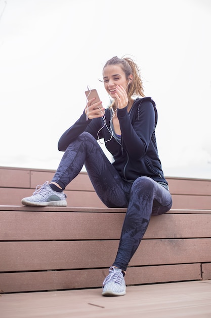 I giovani misura la donna sportiva che riposa e ascolta la musica sul telefono cellulare dopo l'addestramento