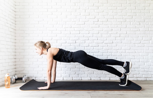 Foto giovane donna adatta in abiti sportivi neri facendo push up a casa