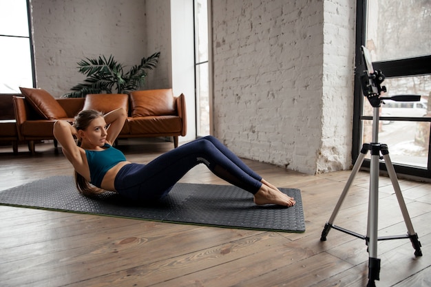 Young fit woman blogger in sportswear shoots video on phone as she does exercises at home in the living room. High quality photo