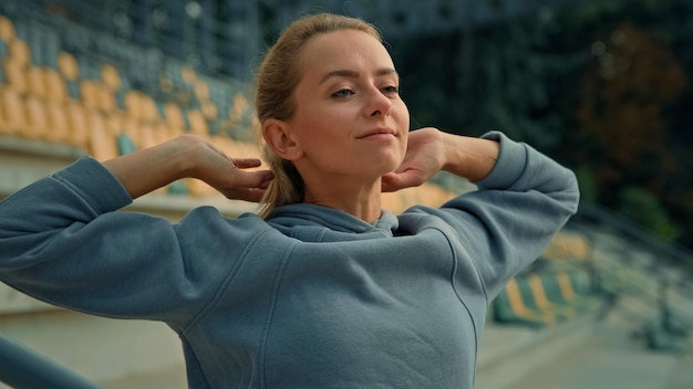 Young fit woman doing aerobics exercise alone on stadium put hands behind head stretching back