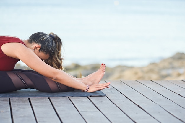 Young fit woman doing stretching exercises for legs against the sea.