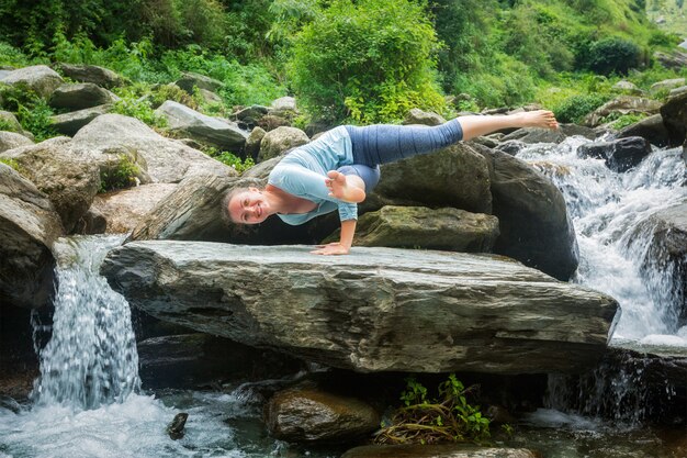 Young fit woman doing yoga oudoors at waterfall