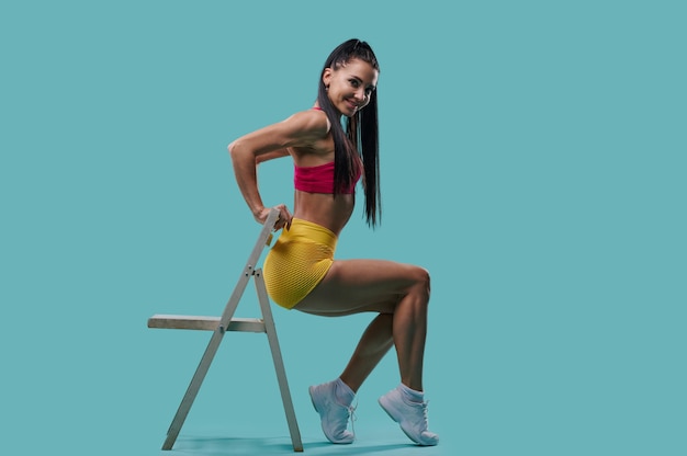 Young fit woman exercises with a chair on the triceps