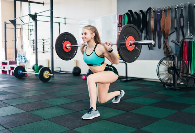 Young fit woman lunges legs with barbell on the shoulders in the gym