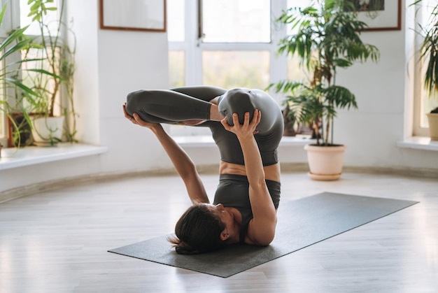 Giovane donna in forma pratica yoga facendo asana in studio di yoga leggero con pianta della serra