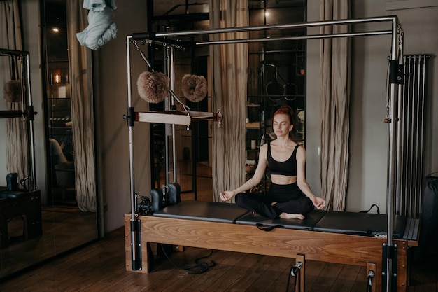 Photo young fit woman sitting in lotus position on trapeze table