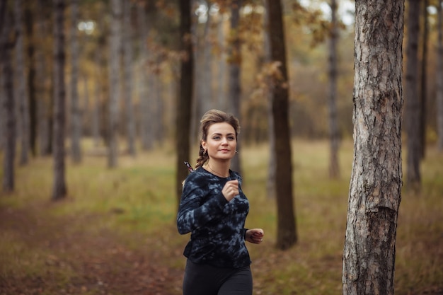 Young fit woman in sportswear runs along forest path