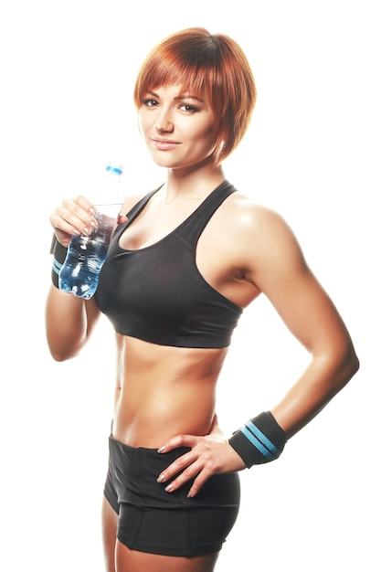 Young fit woman standing and looking at camera, wearing straps with bottle of water. Isolated, white background, studio shot.