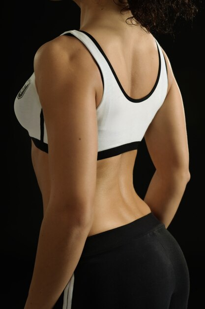 Young fit woman with dumbbells on a black background,back view