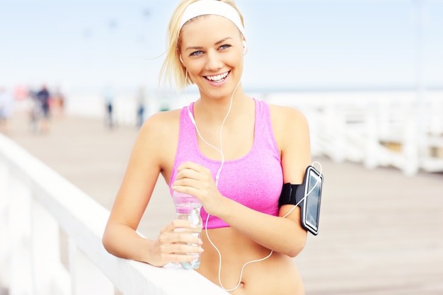 Young fit woman with water on the pier in pink sports bra and white band