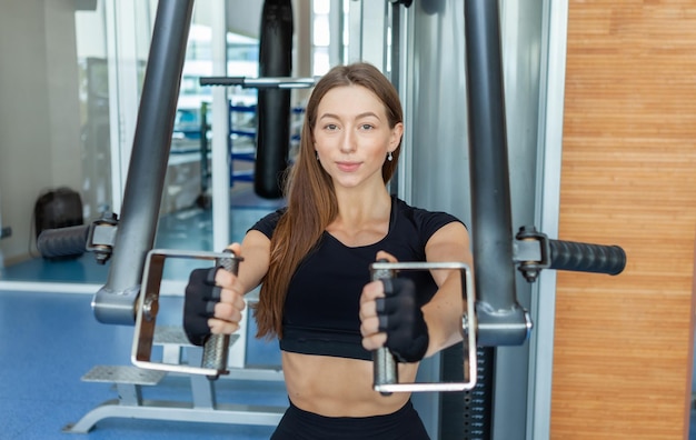 ペックデッキマシンでジムで運動している若いフィットの女性。胸と肩のトレーニング