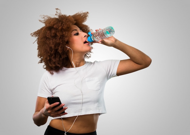 Giovane donna afro fitness in possesso di un mobile e acqua potabile allo stesso tempo