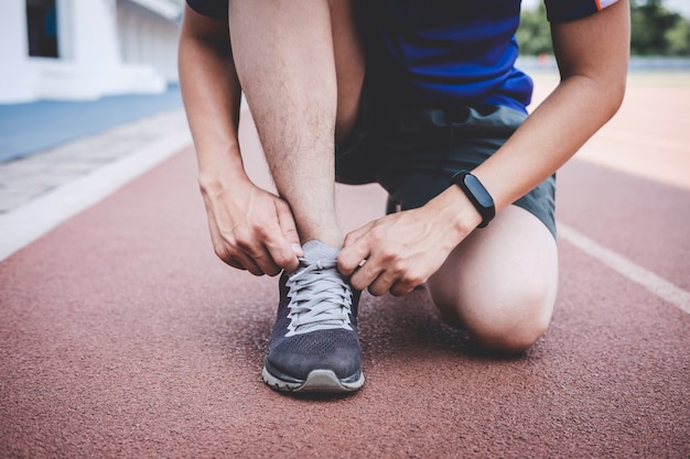 young fitness athlete man running on road track, exercise workout wellness and runner tying shoelaces before run