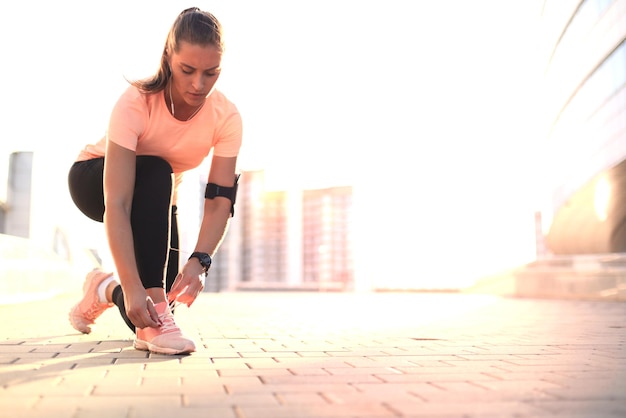 Молодая фитнес-привлекательная спортивная девушка-бегун завязывает шнурки на своей спортивной обуви, готовясь к бегу