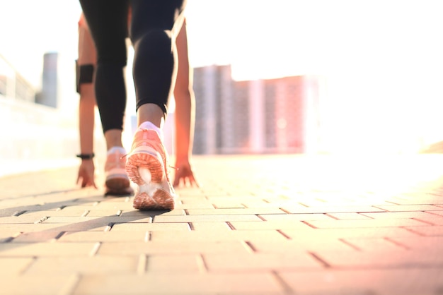 Foto giovane ragazza sportiva attraente di fitness in posizione di partenza all'aperto al tramonto o all'alba in città.