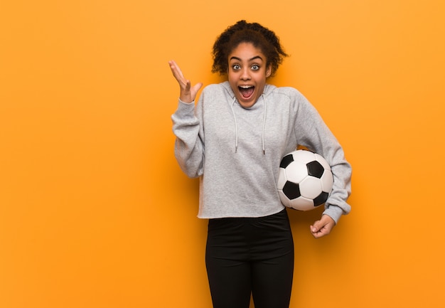 若いフィットネス黒人女性の勝利または成功を祝います。サッカーボールを保持しています。