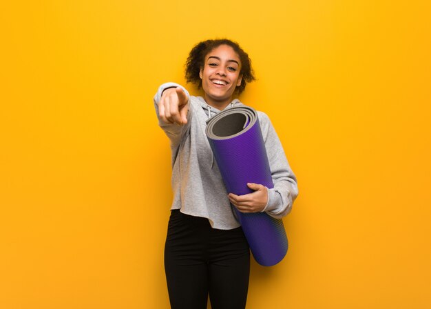 Young fitness black woman cheerful and smiling. Holding a mat.