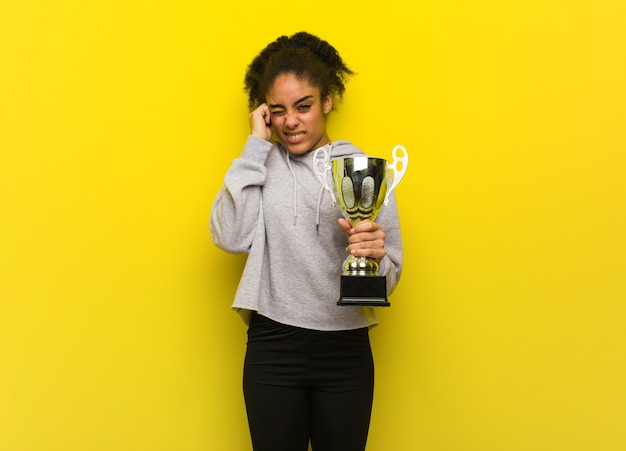 Photo young fitness black woman covering ears with hands. holding a trophy.