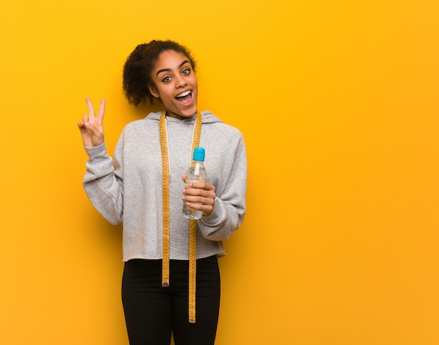 Photo young fitness black woman doing a gesture of victory.holding a water bottle.