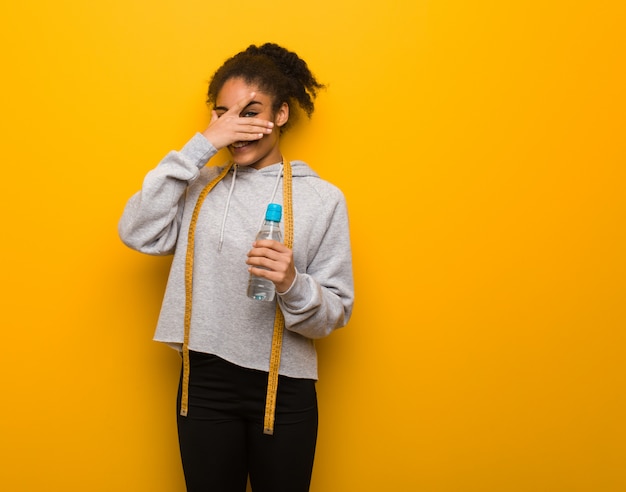 Foto giovane donna di colore fitness imbarazzata e ridendo allo stesso tempo. tenendo una bottiglia d'acqua.