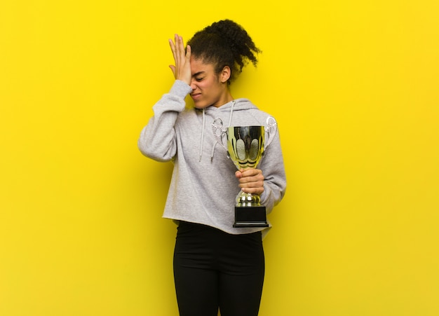 Photo young fitness black woman forgetful, realize something. holding a trophy.