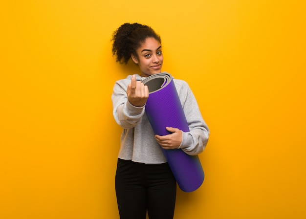 Young fitness black woman inviting to come. Holding a mat.