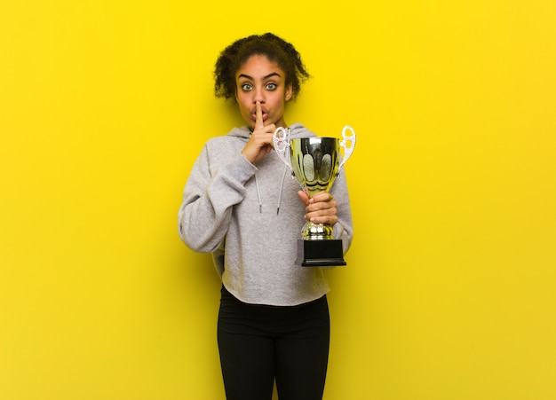 Young fitness black woman keeping a secret or asking for silence. holding a trophy.