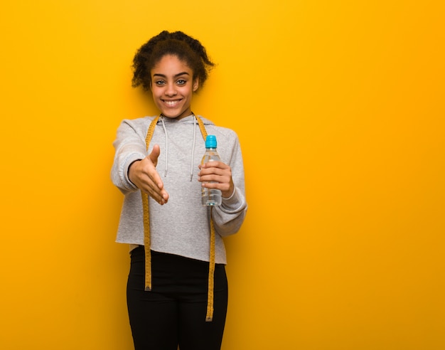 Young fitness black woman reaching out to greet someone, holding a water bottle.