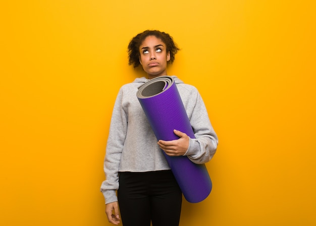 Young fitness black woman tired and bored. holding a mat