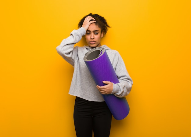 Young fitness black woman tired and very sleepy. Holding a mat.