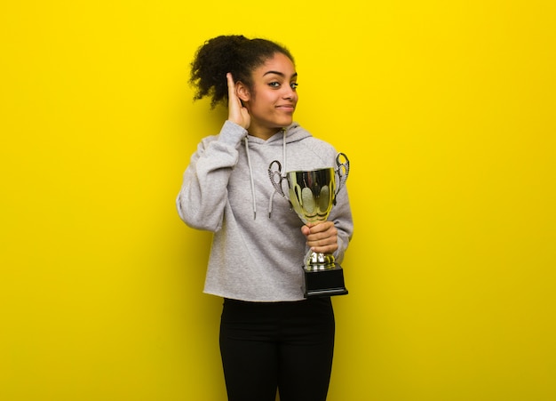 Photo young fitness black woman try to listening a gossip. holding a trophy.