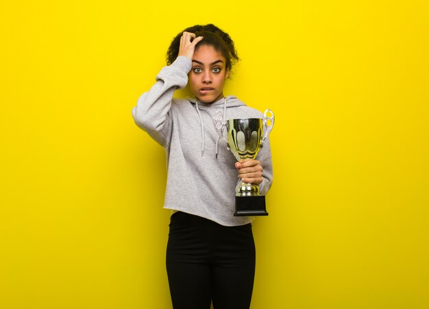 Young fitness black woman worried and overwhelmed. Holding a trophy.