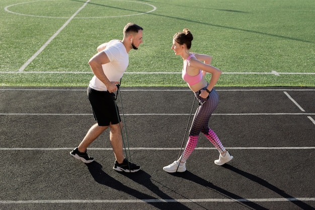 若いフィットネスカップルは、弾力性のあるエキスパンダーで夏にスタジアムでトレーニングします