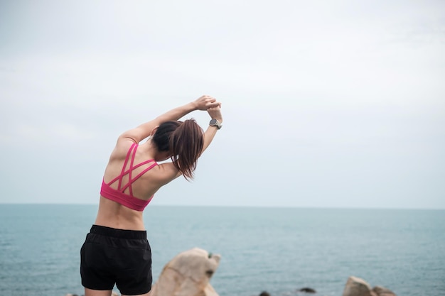 바다 전망을 배경으로 몸을 쭉 뻗는 운동복을 입은 젊은 피트니스 여성, 아침에 건강한 여성 운동. 운동, 웰빙 및 일과 삶의 균형 개념