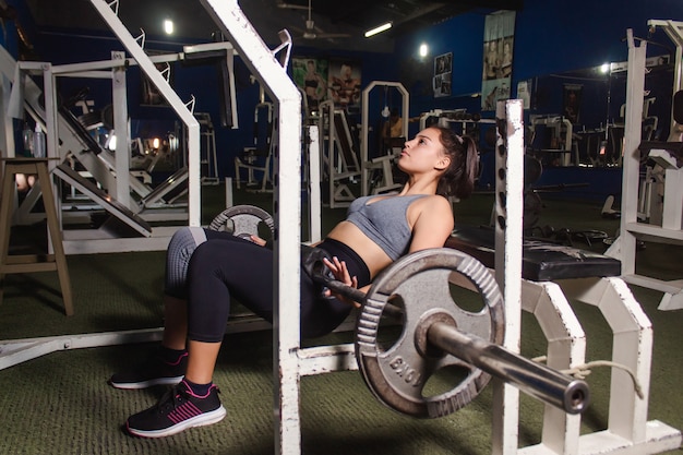 Young fitness girl doing glute exercise with barbell in gym.