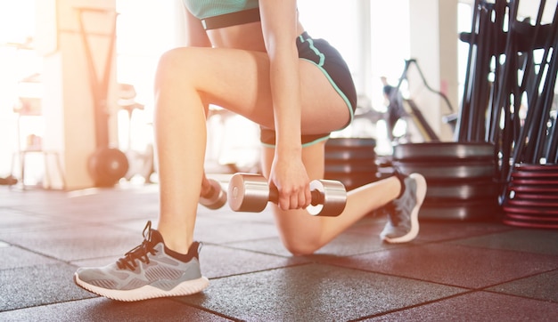 Young fitness girl doing lunges for legs with dumbbells in her hands in the gym.