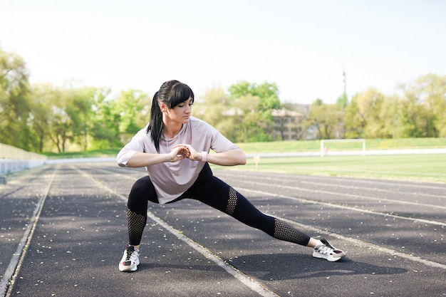 Young fitness girl doing stretching on the stadium. Summer sport activity 