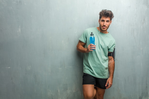 Young fitness man against a grunge wall cheerful and with a big smile, confident