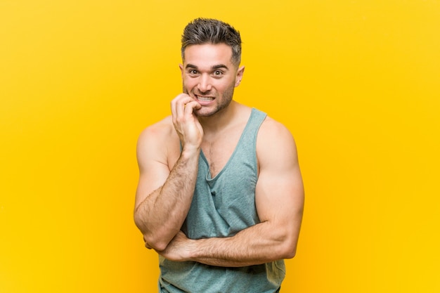 Young fitness man against a yellow wall biting fingernails, nervous and very anxious.