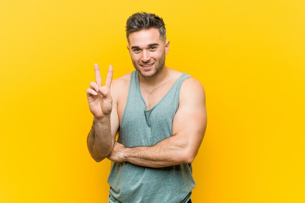 Young fitness man against a yellow wall showing number two with fingers.