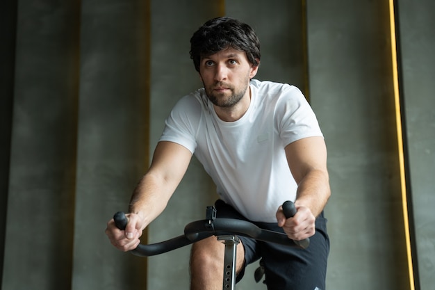 Giovane uomo di forma fisica che esercita il suo allenamento cardio gambe in bicicletta in palestra uomo che lavora su spinning bike in palestra